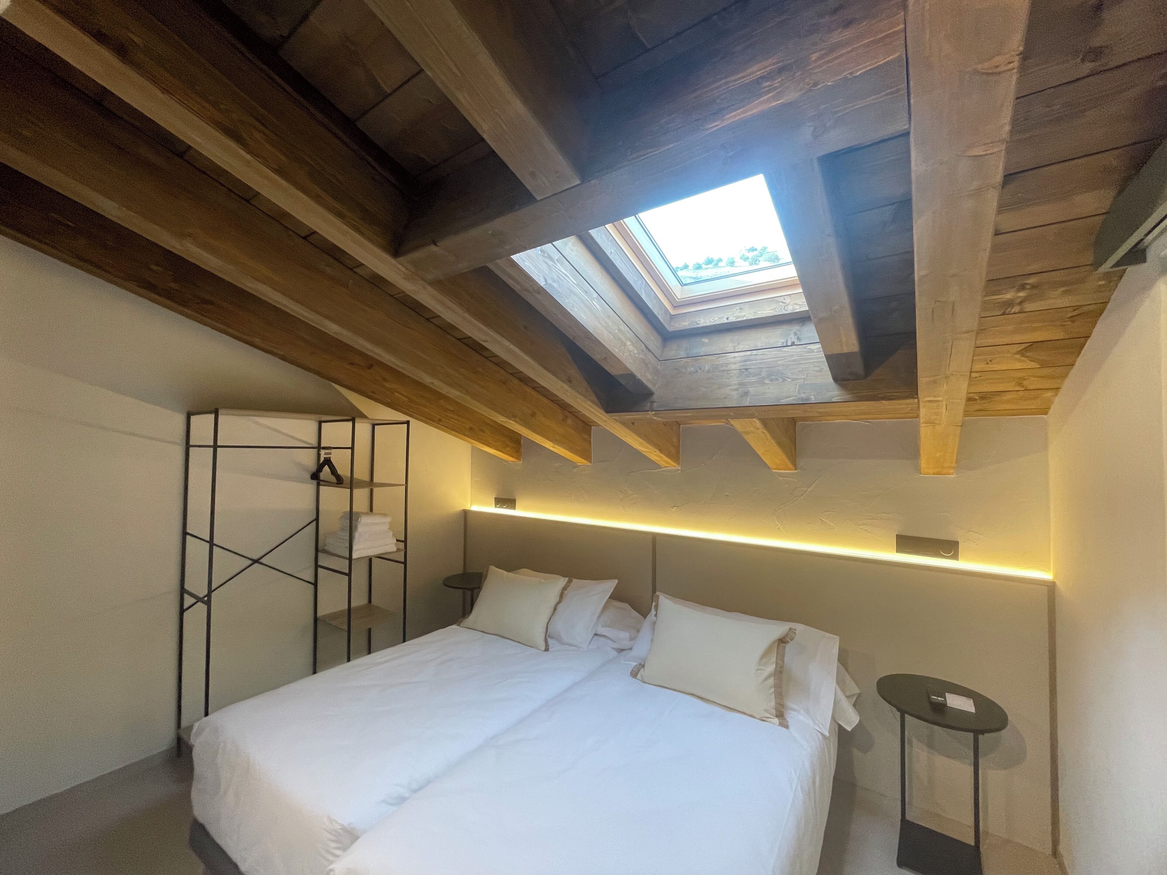 Un dormitorio con tragaluz, una cama, mesitas de noche y una estantería en la pared.