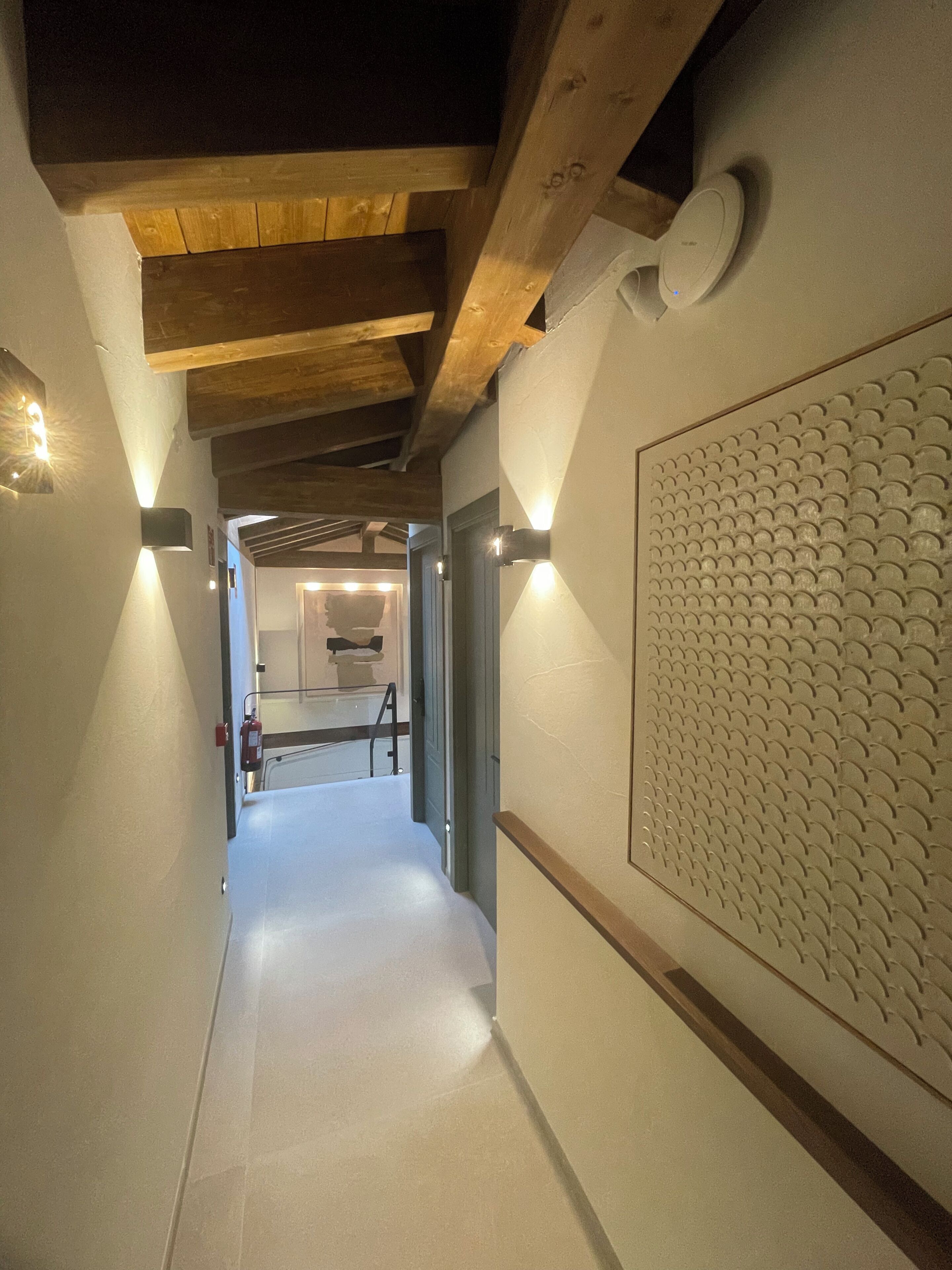 A hallway with wooden beams, a textured wall, and a door leading to a room.
