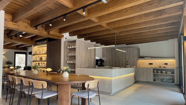 A modern kitchen with a central island, wooden ceiling beams, and a dining area with chairs and a table.
