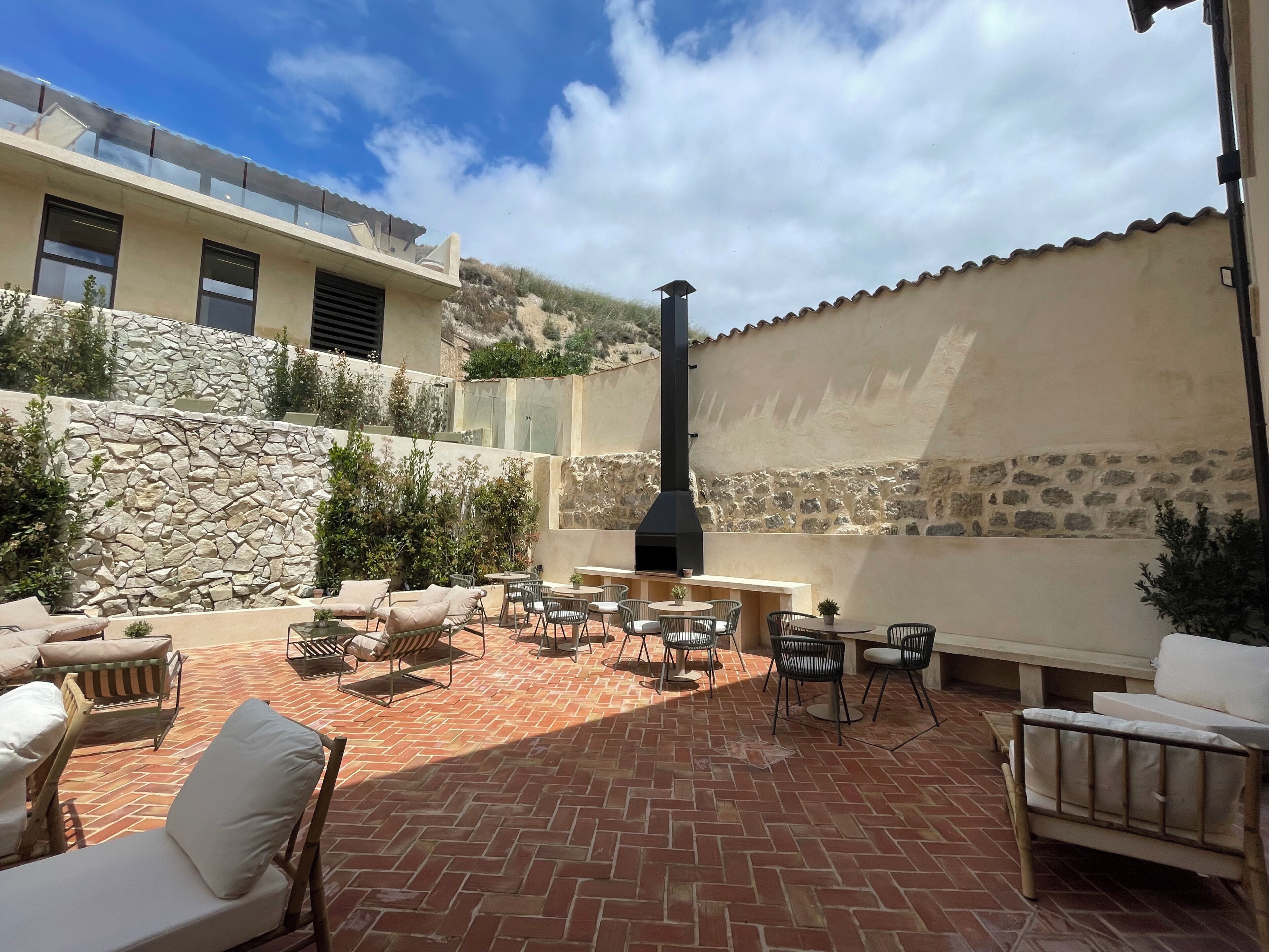 Un patio con mobiliario exterior, un muro de piedra y una chimenea.