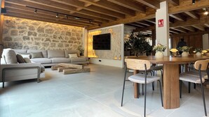 A modern living room with a stone wall, a large flat-screen TV, a wooden dining table with chairs, and a sofa.