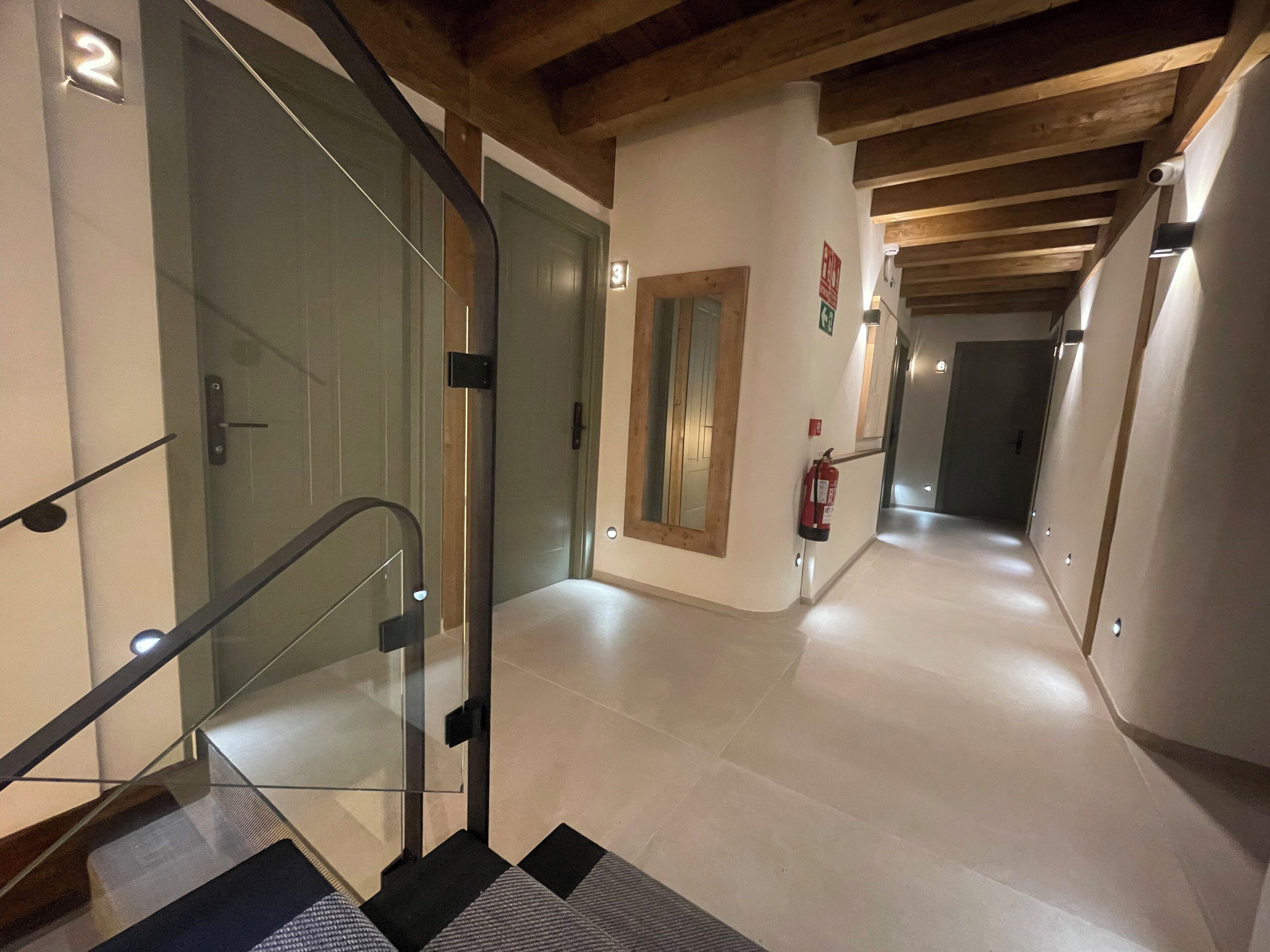 Interior moderno com elevador de vidro, extintor de incêndio e corredor que dá para outro espaço.