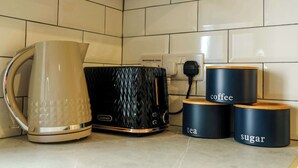 Een keuken met een waterkoker, een magnetron en drie voorraadpotten met koffie, thee en suiker.
