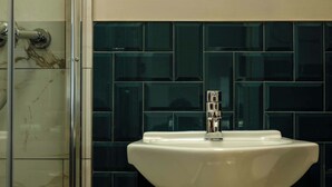 Een badkamer met een wit wastafelmeubel, donker betegelde wanden en een douchecabine van glas.