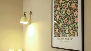 Een lijst met een kunstwerk getiteld 'William Morris Fruit Patroon' hangt aan een muur.