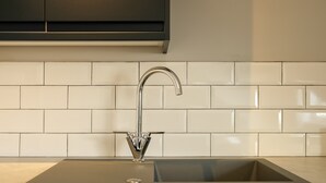 A modern kitchen with a stainless steel sink, white tiled backsplash, and dark cabinetry. - The Willow - Studio 14 (Patchway)