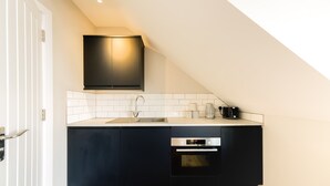 A modern kitchen with a black countertop, white tiled backsplash, and a built-in oven. - The Willow - Studio 14 (Patchway)