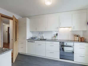 A modern kitchen with white cabinetry, a granite countertop, and a dishwasher. - Plazzöl 111B, (Ftan) by Interhome (Ftan)