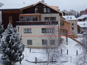 A multi-story building with a wooden facade, balconies, and a snow-covered environment. - Plazzöl 111B, (Ftan) by Interhome (Ftan)