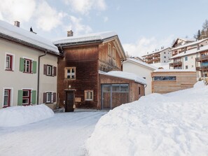 A snow-covered building with a wooden facade, a garage, and a small porch. - Plazzöl 111B, (Ftan) by Interhome (Ftan)