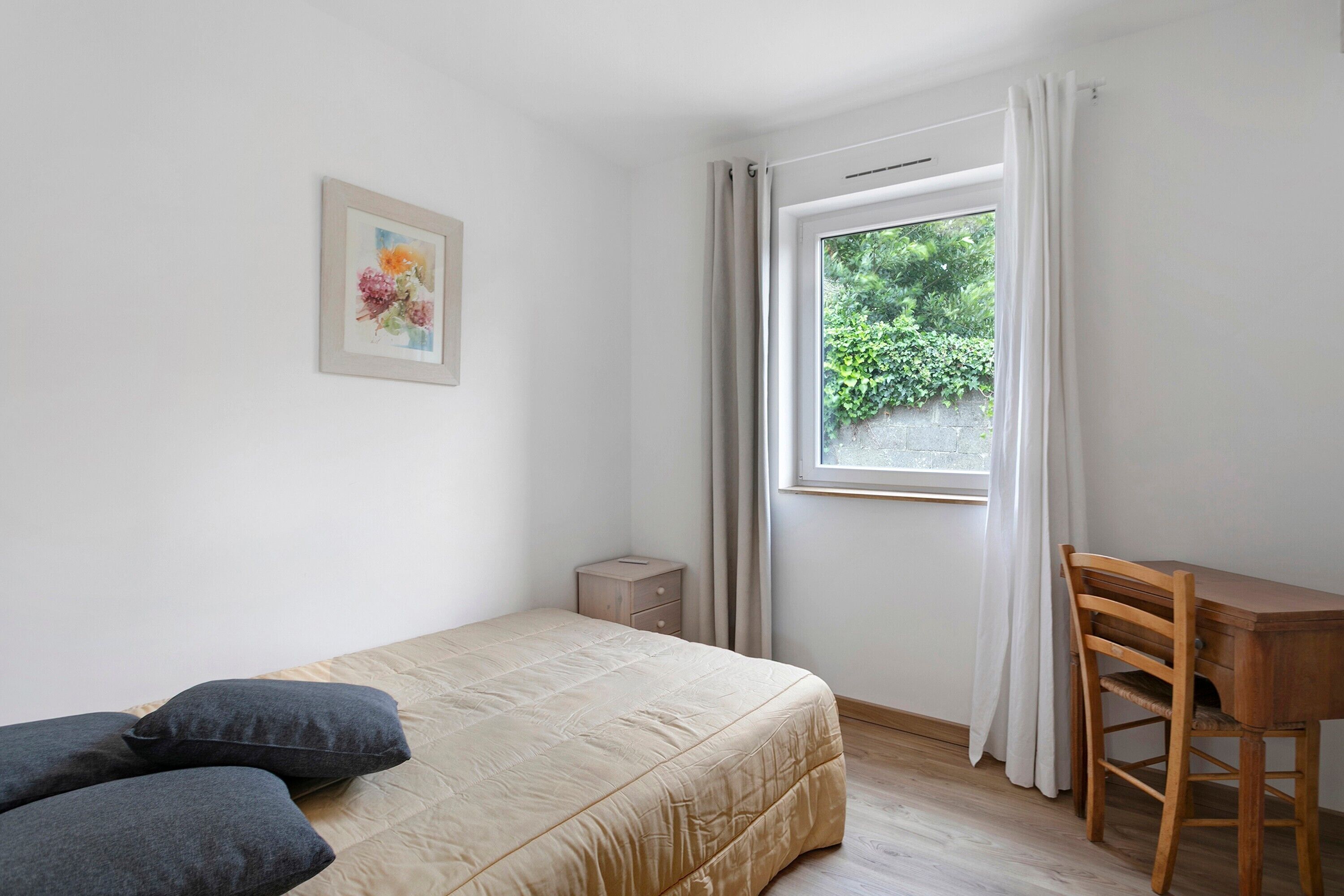 Un dormitorio con cama, escritorio, silla, mesita de noche y ventana con cortinas.