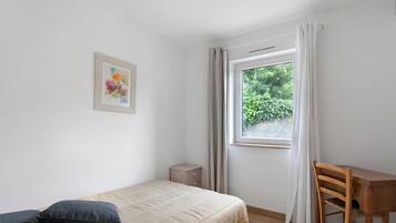 Un dormitorio con cama, escritorio, silla, mesita de noche y ventana con cortinas.