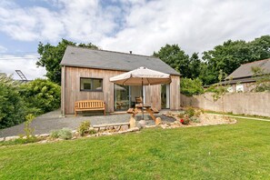 A wooden house with a patio, a bench, and an umbrella.