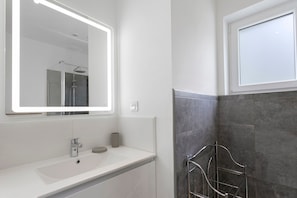 A modern bathroom with a white vanity, a large mirror, a shower area, and a towel rack.