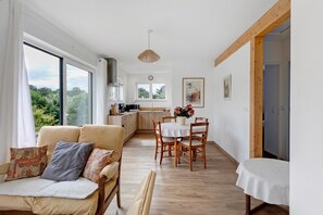 A cozy living room with a sofa, a dining table with chairs, and a kitchen in the background.