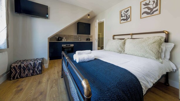 Ein Schlafzimmer mit Bett, Flachbildfernseher, Küchenzeile und Bildern an den Wänden.