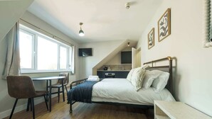 Ein Schlafzimmer mit einem Bett, einem Schreibtisch, einem Sessel, einem Fernseher und einem Fenster.