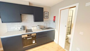 A compact kitchen with dark cabinets, a white countertop, a built-in dishwasher, and a tiled backsplash.