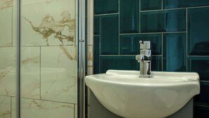A bathroom with a white sink, a chrome faucet, and a tiled wall with a marble pattern. - The Willow - Flat 10 (Patchway)