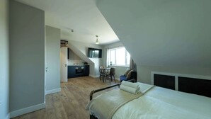 A bedroom with a bed, a desk, and a kitchenette in the background. - The Willow - Studio 23 (Patchway)