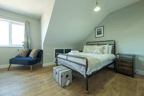 A bedroom with a bed, a chair, a bedside table, and a window. - The Willow - Studio 23 (Patchway)