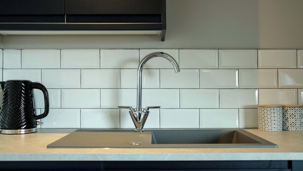 A modern kitchen with a stainless steel sink, white tiled backsplash, and black cabinets. - The Willow - Studio 23 (Patchway)