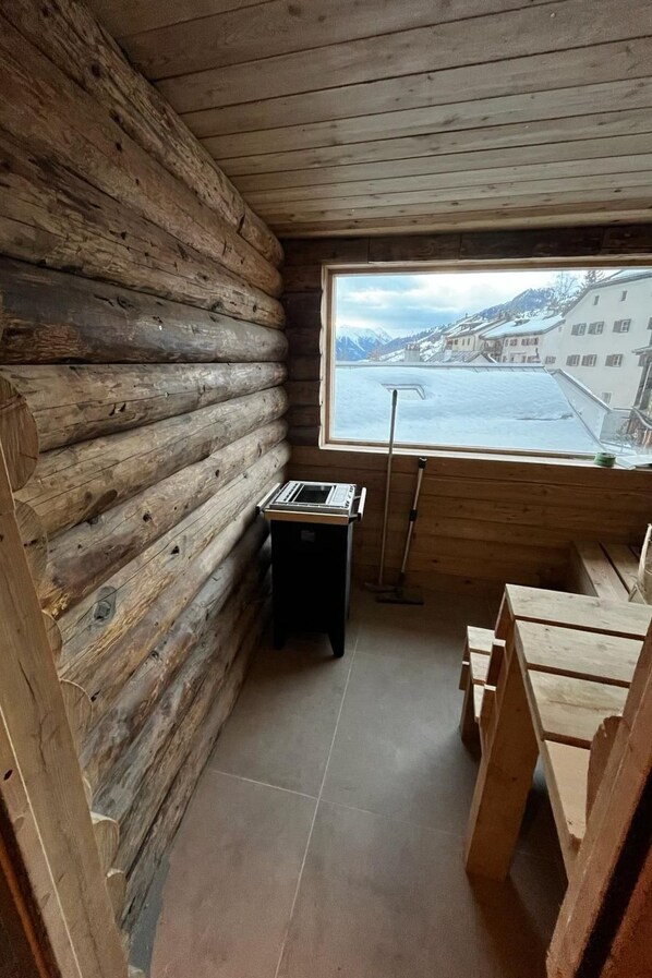 A log cabin with a wooden interior, a window with a view of a snowy landscape, and a small table with a keyboard.