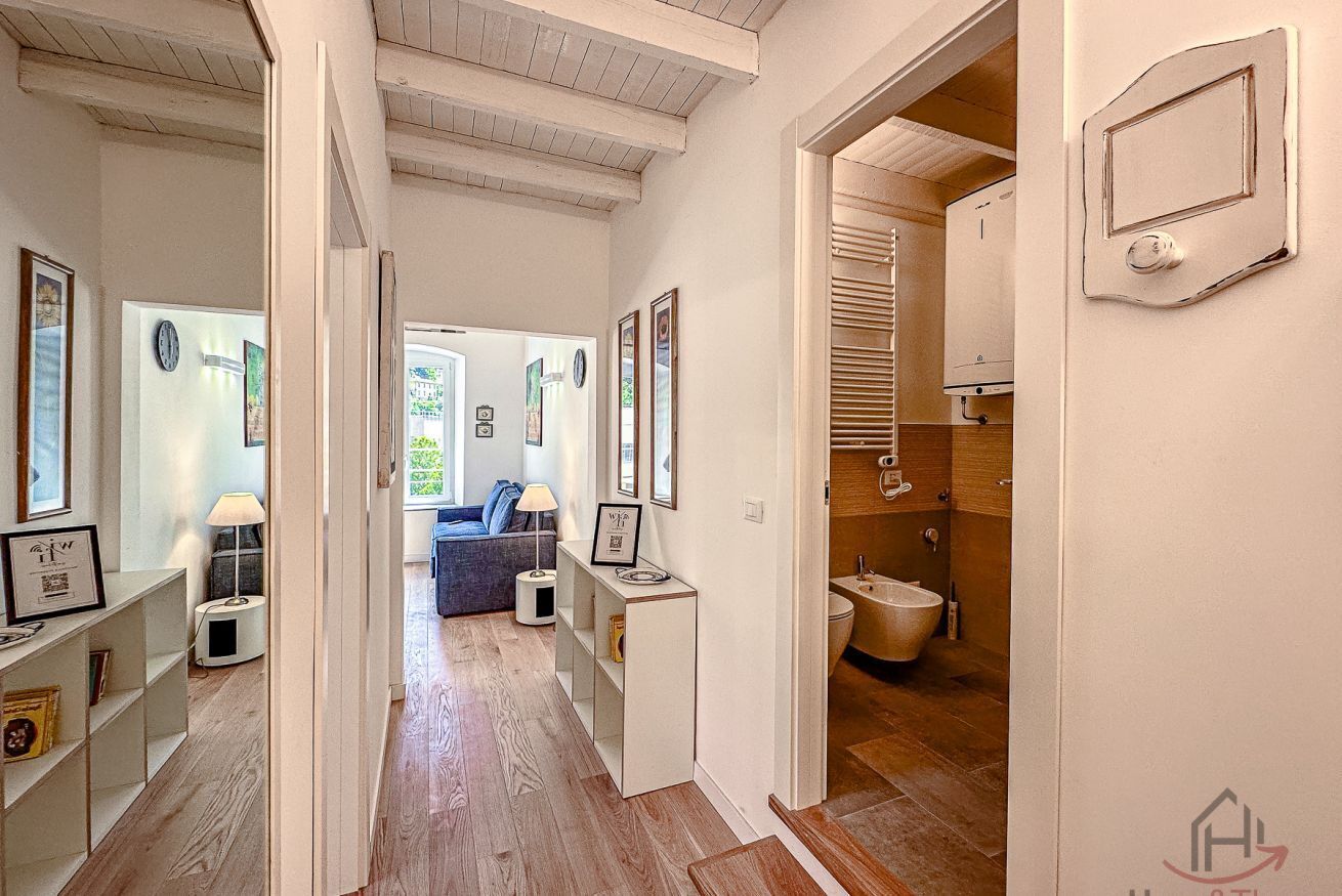 A hallway leading to a living room with a sofa, framed pictures, and a wooden floor.