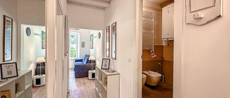A hallway leading to a living room with a sofa, framed pictures, and a wooden floor.