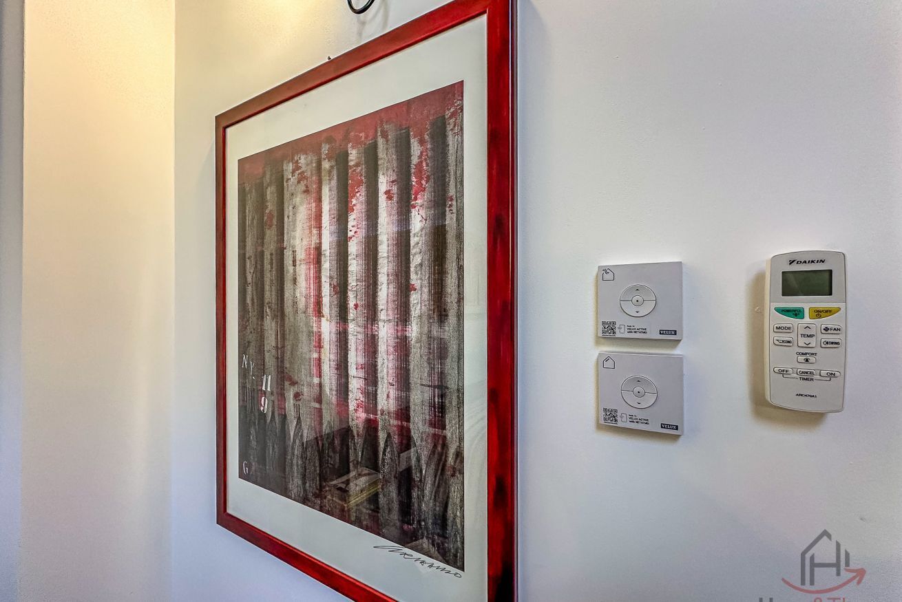 Un tableau abstrait encadré, un thermostat et un panneau de commande fixés sur un mur.