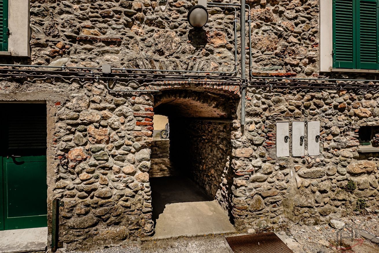 A stone building with a narrow passageway, a green door, and a metal light fixture.