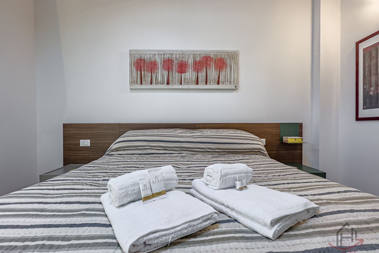 A hotel room with a bed, a wall-mounted artwork, and neatly folded towels on the bed.