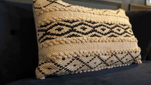 Un coussin orné d’un motif géométrique, posé sur un canapé de couleur foncée.