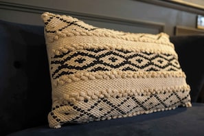 Ein Kissen mit geometrischem Muster auf einer dunkel gefärbten Couch.