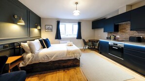 Une chambre d’hôtel de taille réduite, comprenant un lit, une table de chevet, une chaise et un coin cuisine.