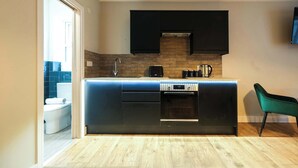 A modern kitchen with a built-in dishwasher, oven, and a black countertop. - The Willow - Studio 27 (Patchway)