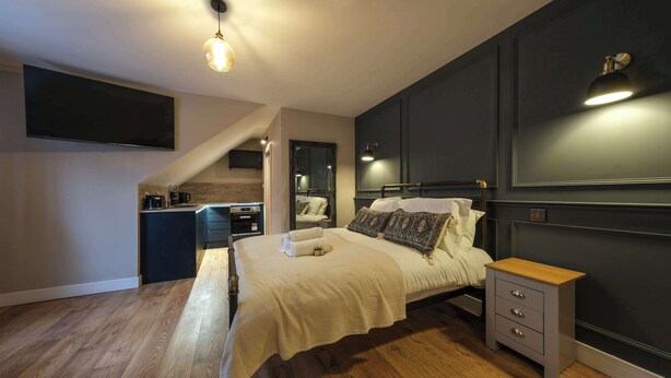 A bedroom with a bed, bedside table, and a small kitchenette area. - The Willow - Studio 33 (Patchway)
