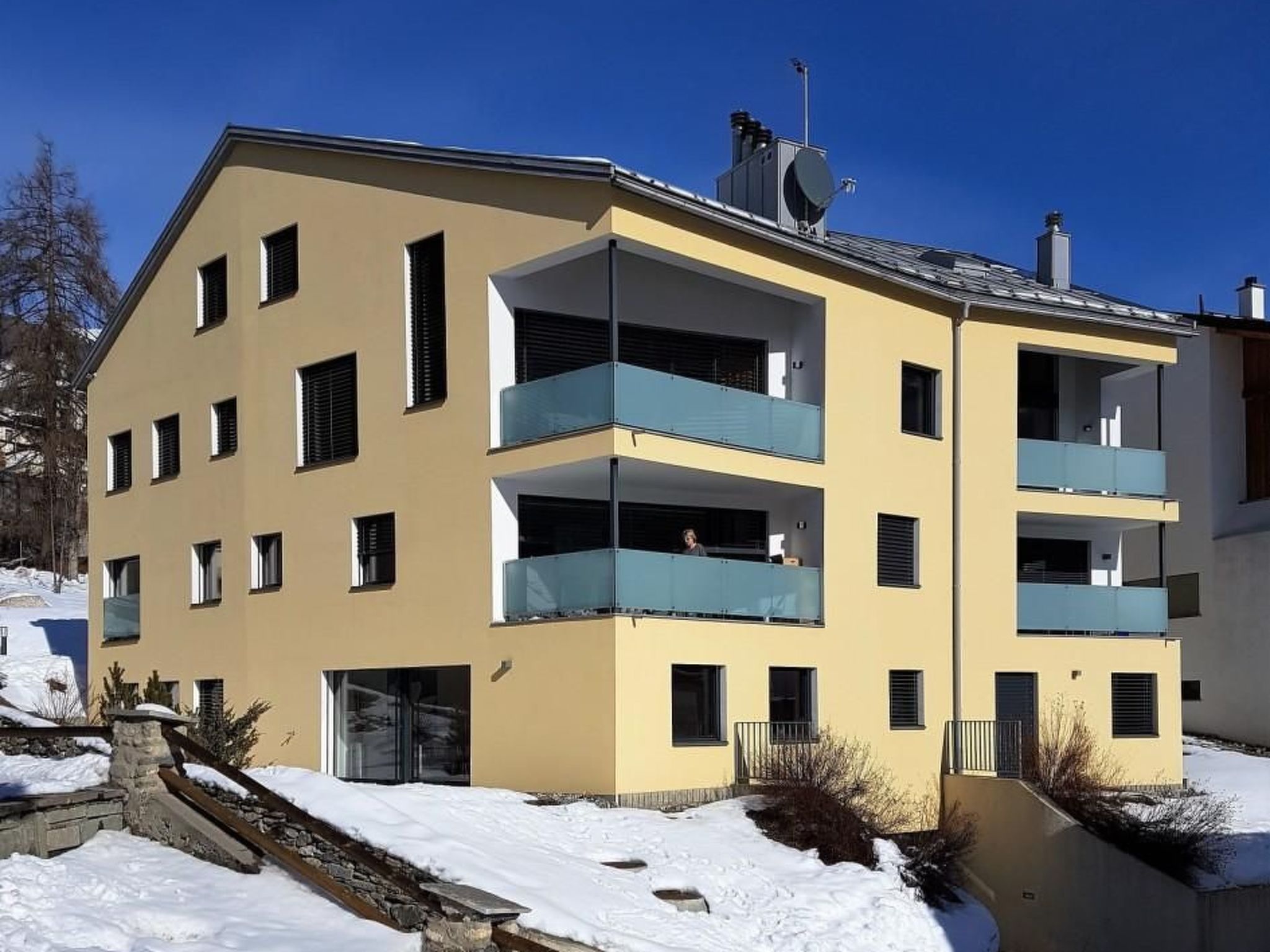 A multi-story building with balconies, a flat roof, and a snow-covered ground.