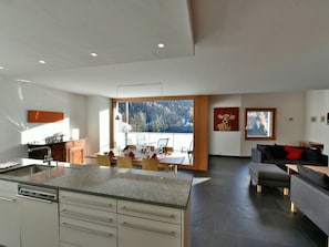 A modern kitchen with a dining area, large windows, and a view of a forest. - CRAISTA 8, (Scuol) by Interhome (Scuol)