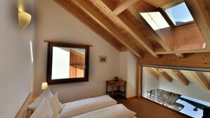 Une chambre avec un plafond en bois, une grande fenêtre et un lit recouvert d’une literie à rayures.