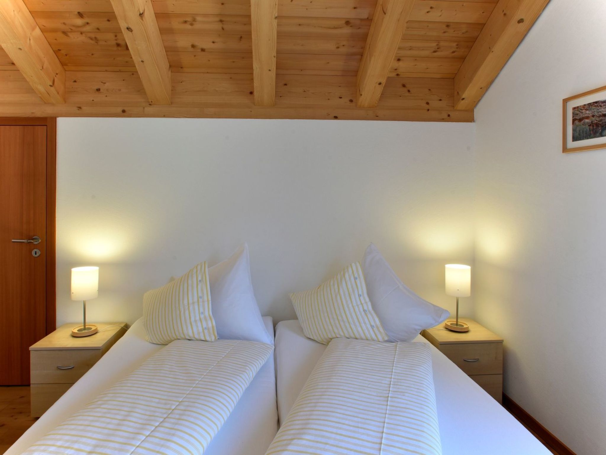A bedroom with two beds, wooden headboard, bedside lamps, and a door.