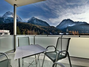 A balcony with a table and chairs, overlooking a mountainous landscape with a church. - CRAISTA 8, (Scuol) by Interhome (Scuol)