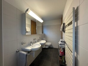 A modern bathroom with two sinks, a toilet, and a towel rack.