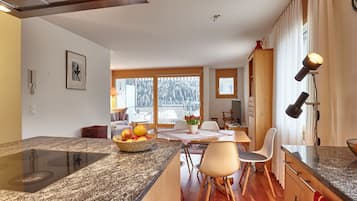 A modern kitchen with granite countertops, a dining area with a table and chairs, and large windows with a view of trees.