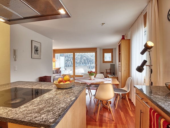 A modern kitchen with granite countertops, a dining area with a table and chairs, and large windows with a view of trees.