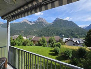 A balcony with a view of a mountain range, a grassy area, and several buildings.