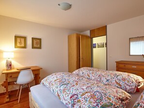 A bedroom with a bed, a desk, a chair, a wardrobe, and a bedside table.