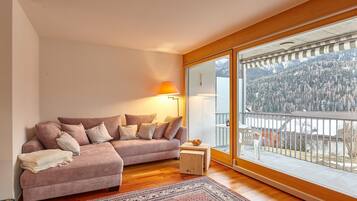 A cozy living room with a sectional sofa, a patterned rug, and a large window offering a mountain view.