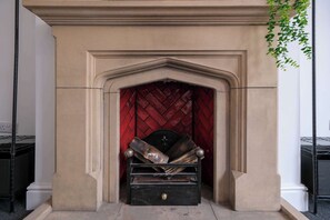 A fireplace with a red herring pattern, a black mantelpiece, and a wooden log storage box.