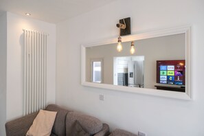 A living room with a sofa, a large mirror, and a television displaying a colorful interface.